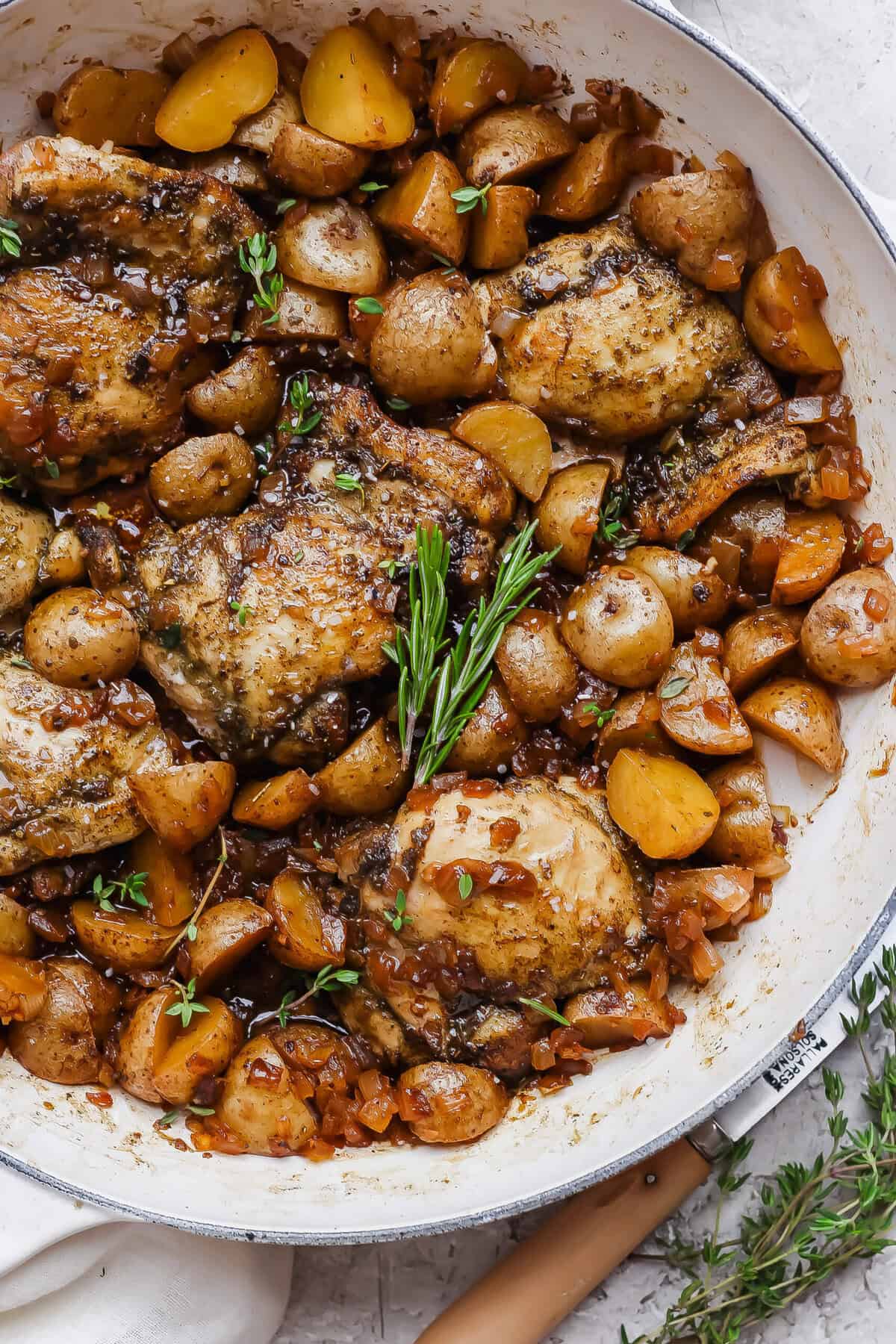 Apple cider chicken thighs nestled with baby potatoes and onion in a glossy skillet sauce.