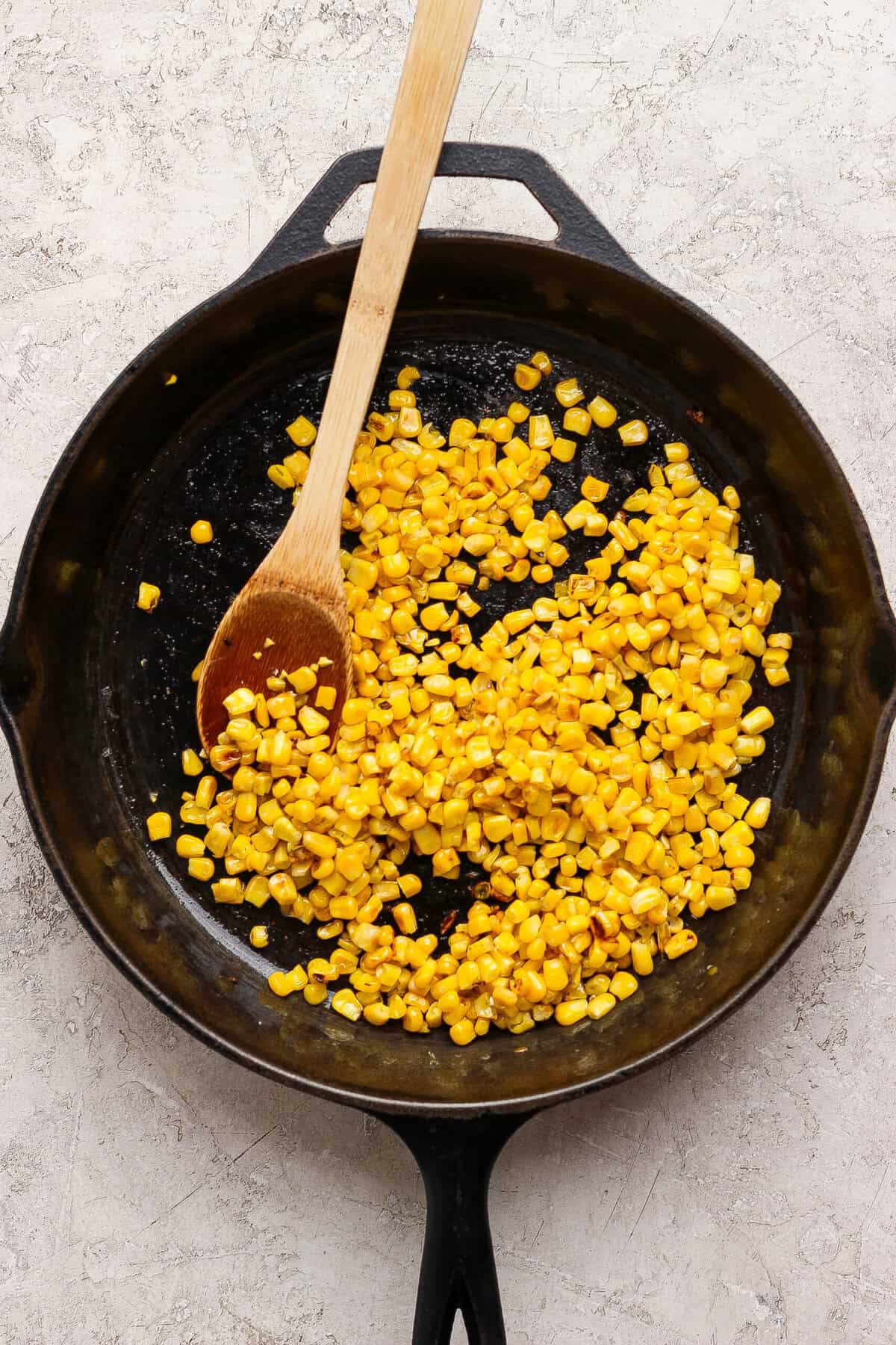 Sweet corn kernels browning in avocado oil in a cast-iron skillet.