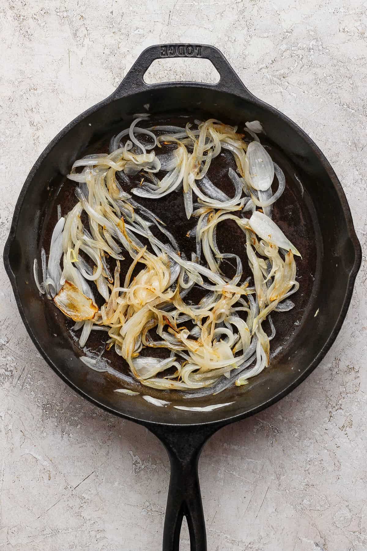 Soft golden sliced onions in a cast-iron skillet for cottage cheese French onion dip.