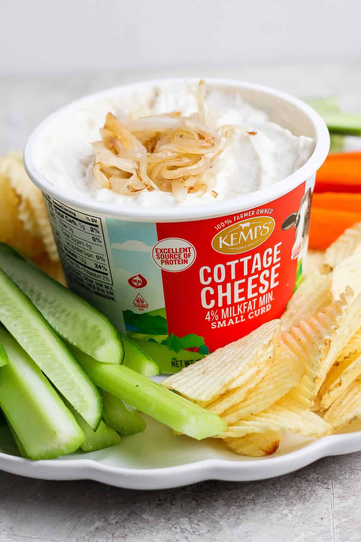 Finished cottage cheese French onion dip topped with golden onions and served in the cottage cheese container with potato chips and celery.