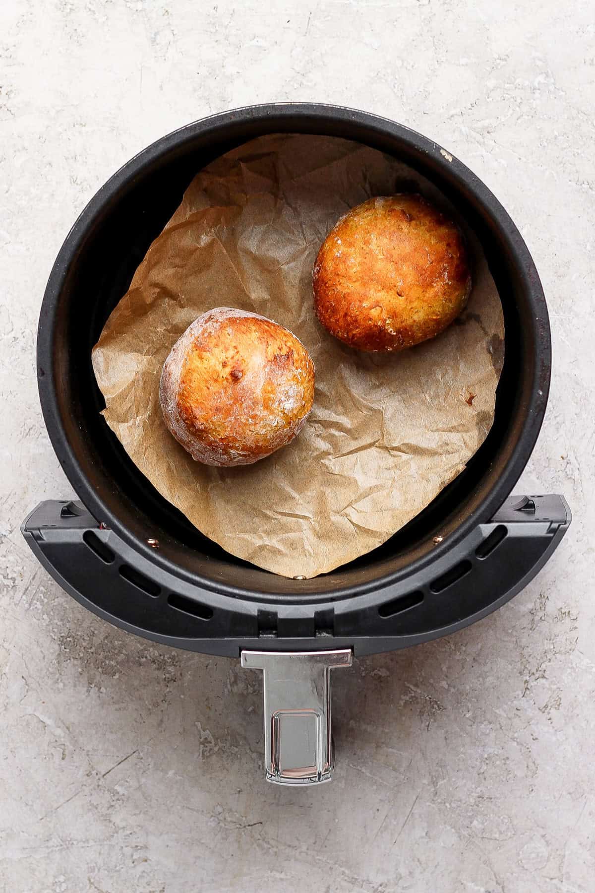 Two golden pumpkin fritters resting on parchment paper in an open air fryer basket.