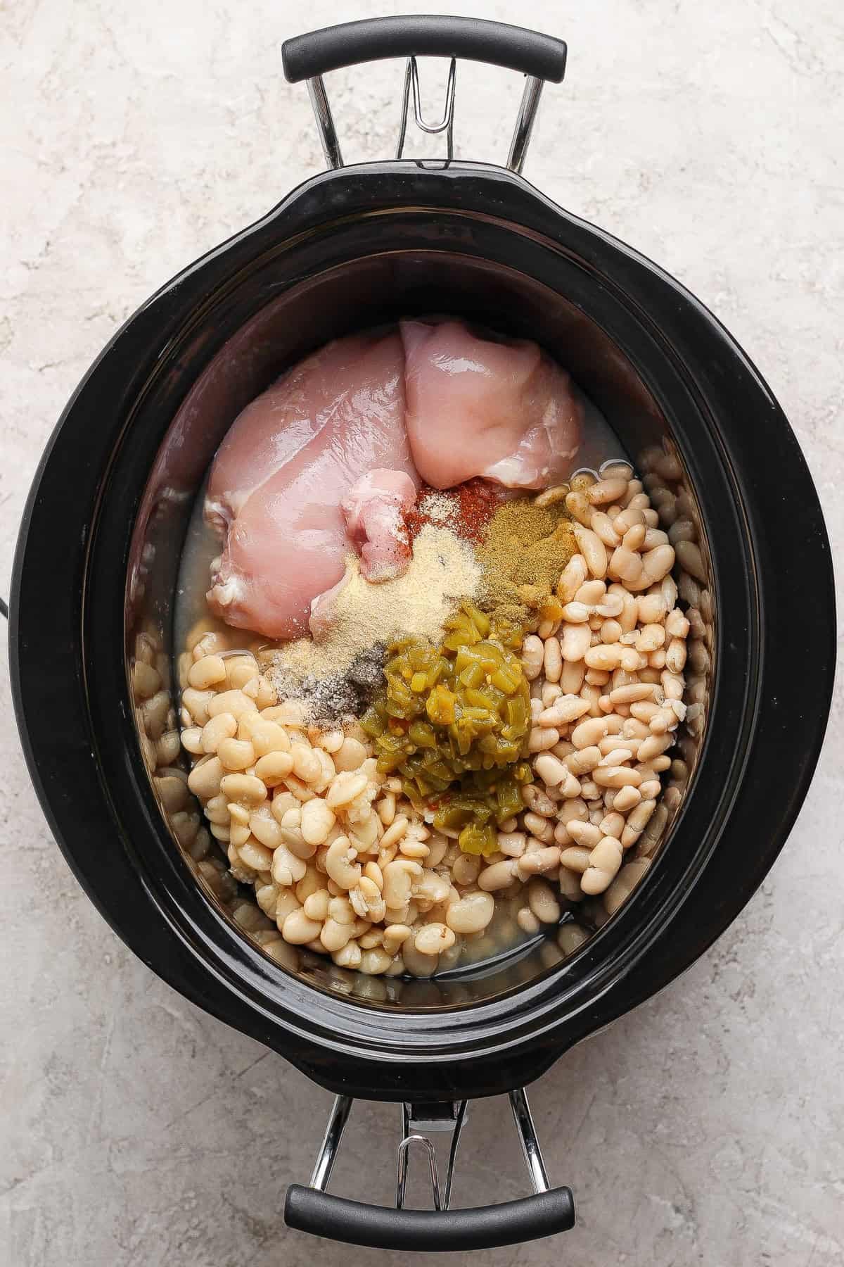 Raw chicken, white beans, green chiles, vinegar, and spices loaded into a slow cooker.