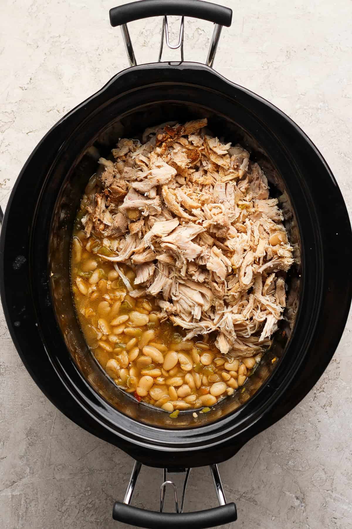 Shredded chicken returned to a slow cooker with butter beans and cannellini beans.