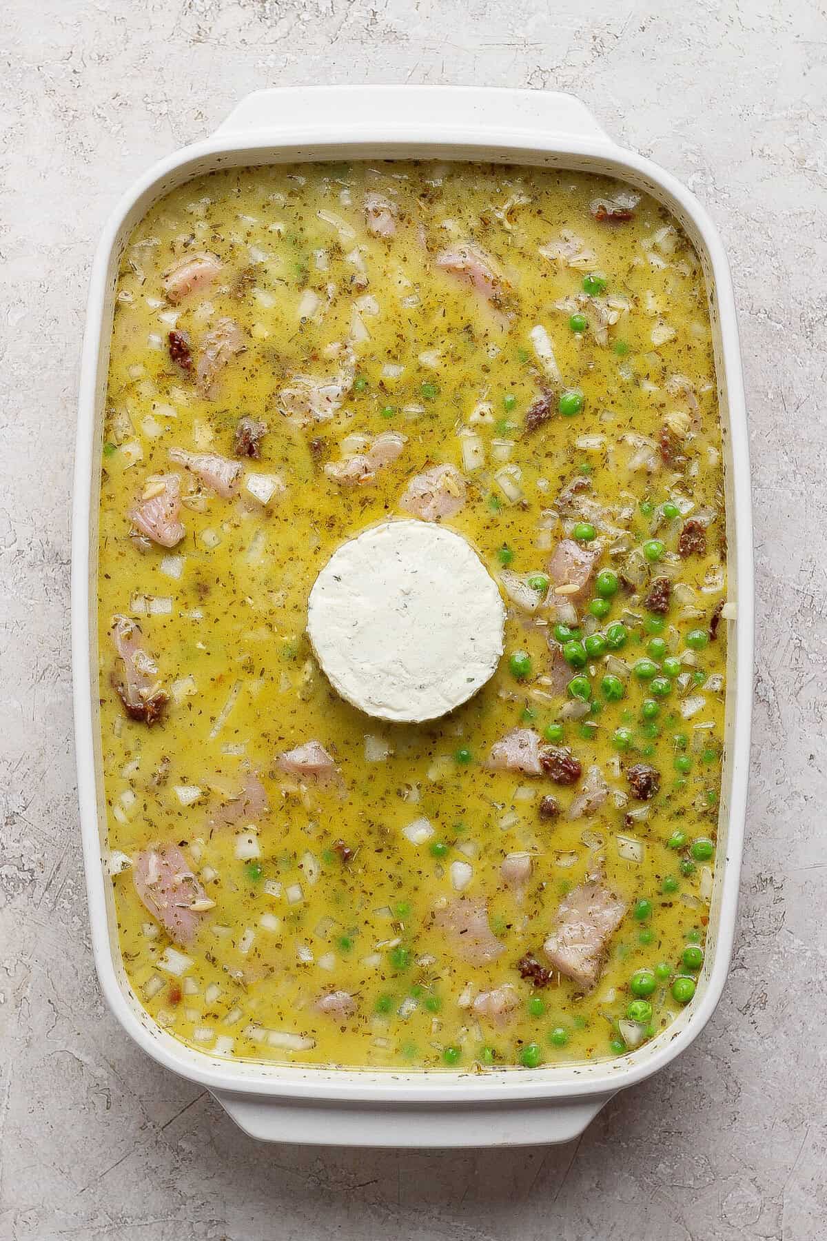 Unbaked chicken pesto orzo mixture in a white casserole dish with a whole puck of Boursin in the center.