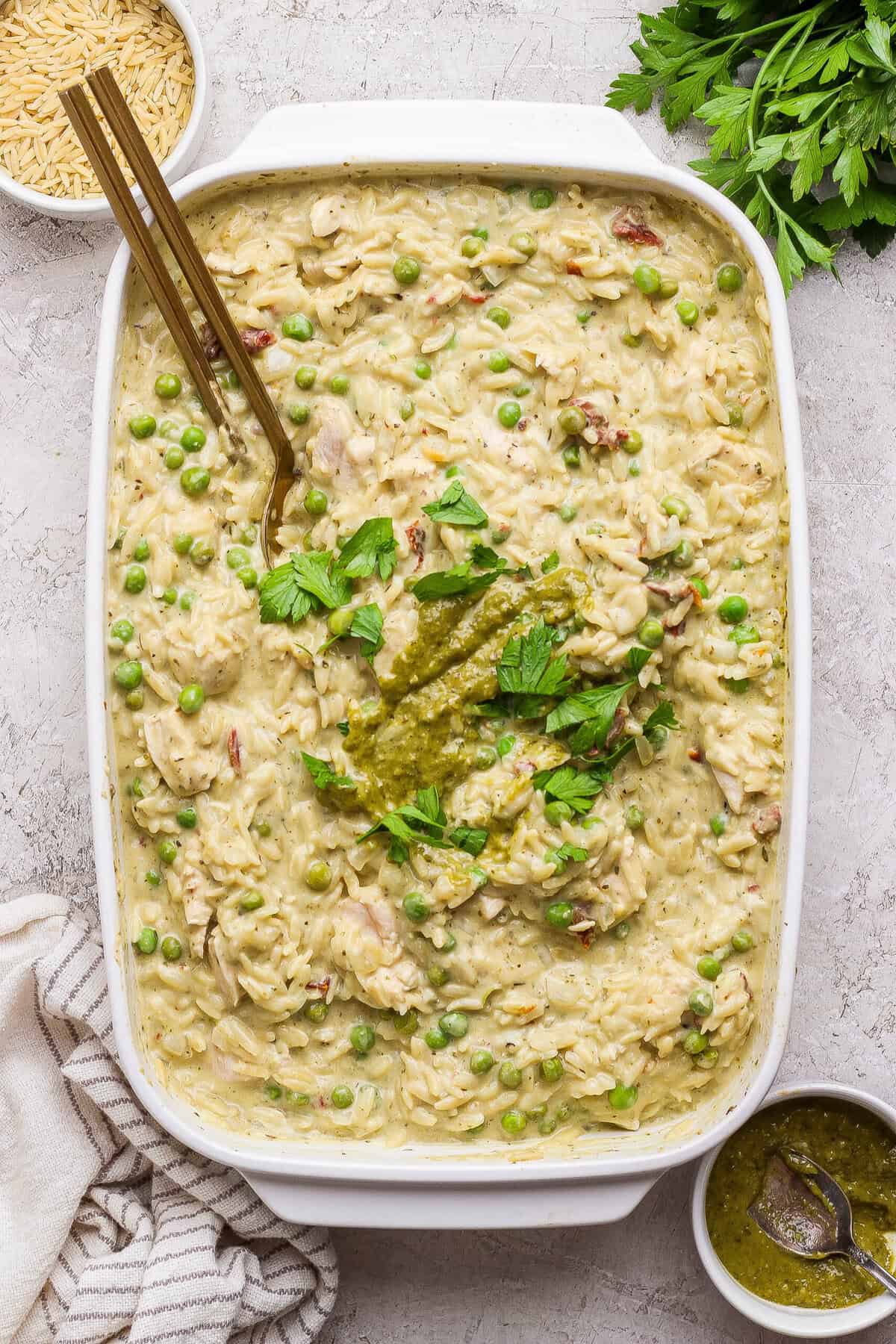Finished creamy chicken pesto orzo casserole garnished with pesto and fresh parsley.