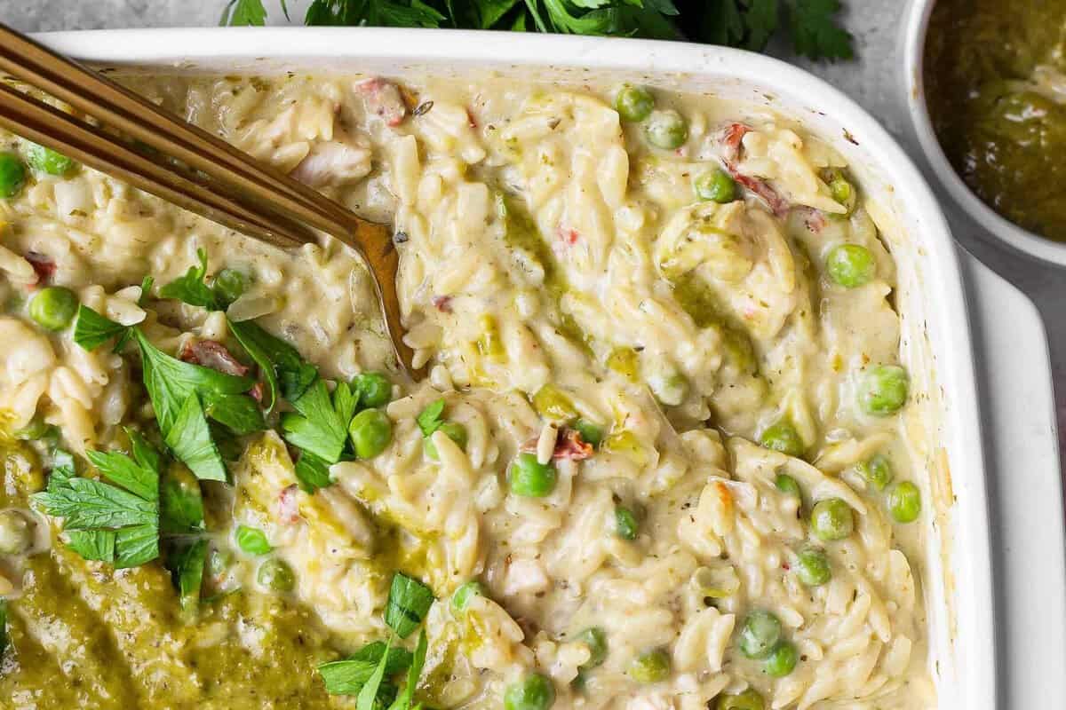 Close-up of creamy chicken pesto orzo with peas, sun-dried tomatoes, pesto, and fresh parsley.