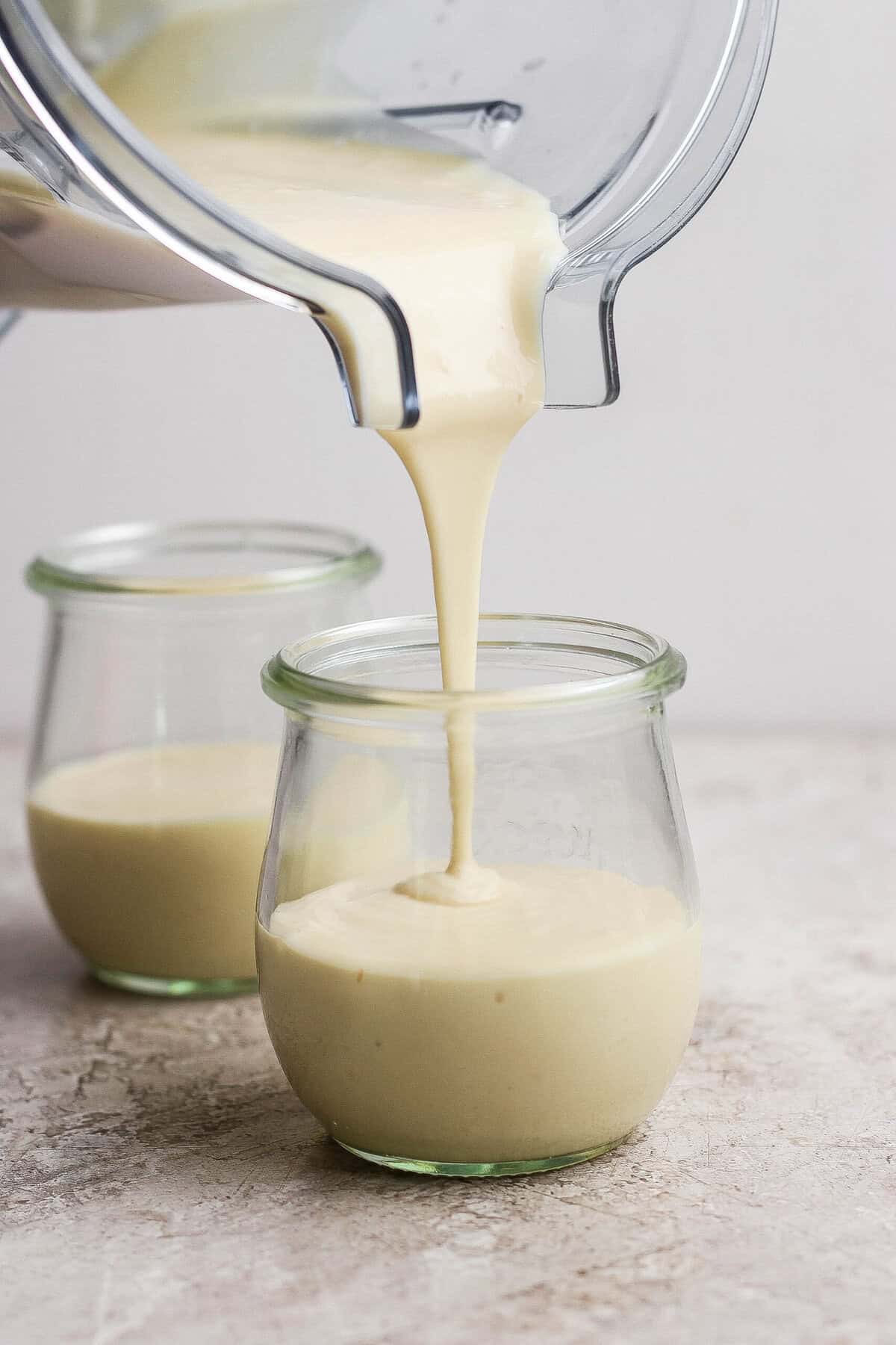 Blended cottage cheese cheesecake mixture being poured into individual clear dessert jars.