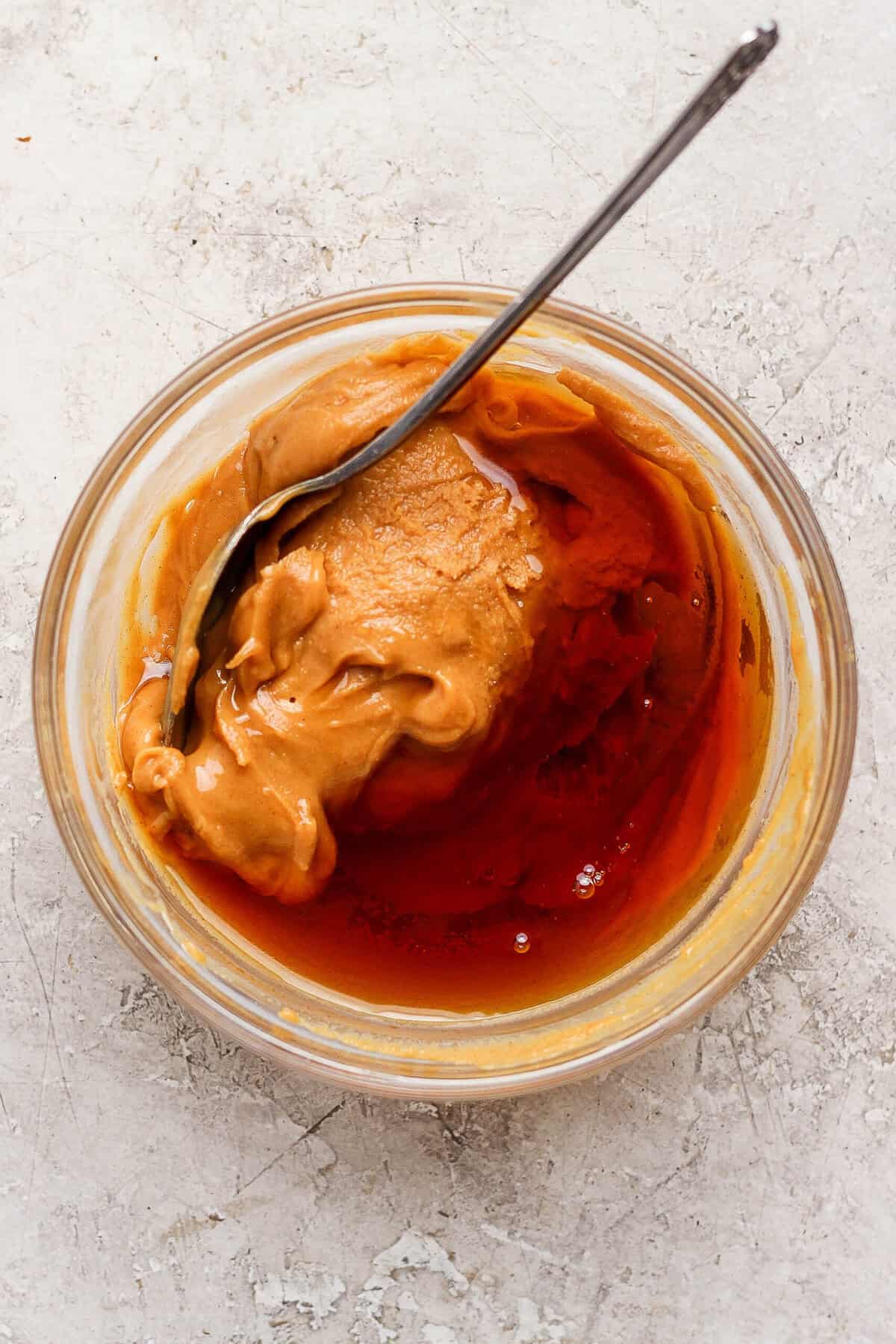 Creamy peanut butter and maple syrup being stirred together in a small glass bowl.