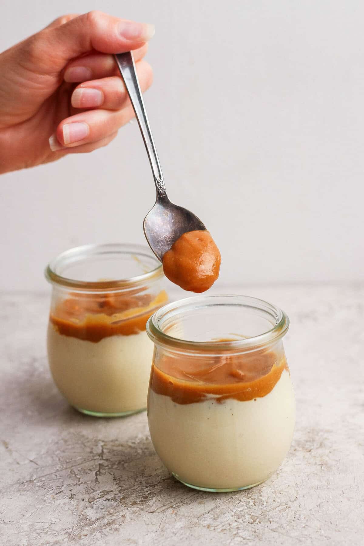 Maple peanut butter being spooned over the cottage cheese layer in individual dessert jars.