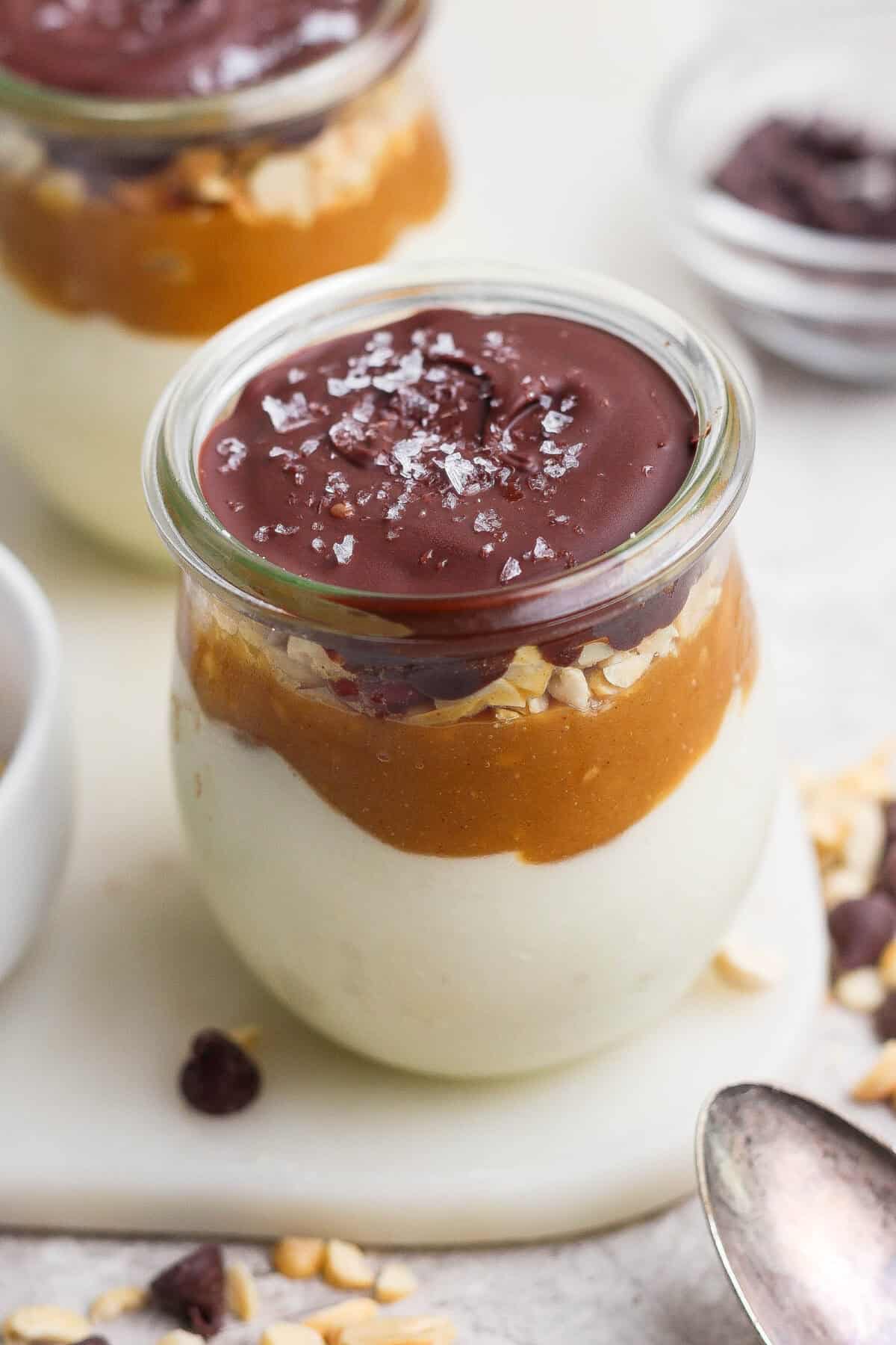 Individual Snickers cheesecake cup layered with blended cottage cheese, maple peanut butter, salted peanuts, and a glossy chocolate shell.