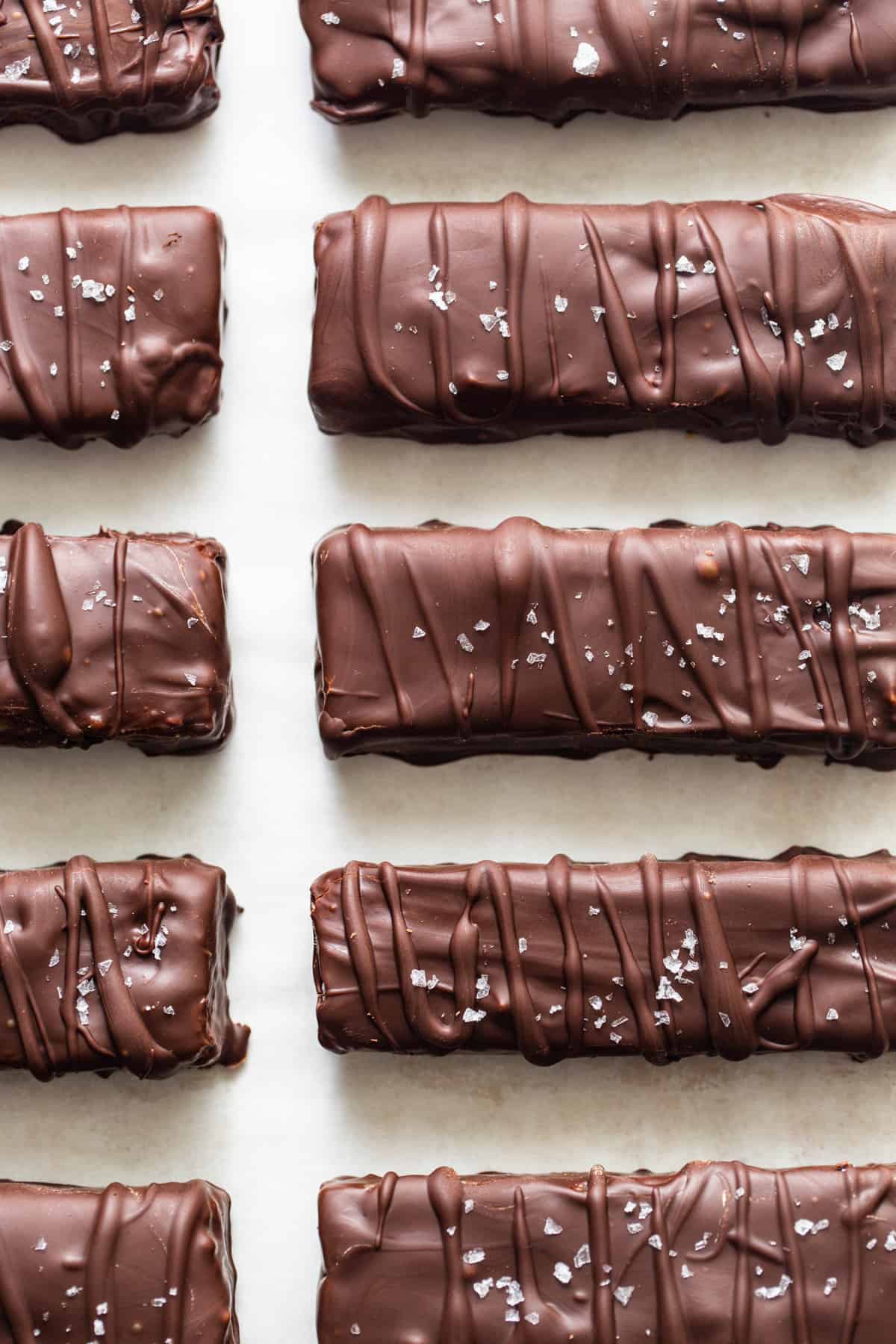 Chocolate-coated protein bars on parchment sprinkled with flaky salt.