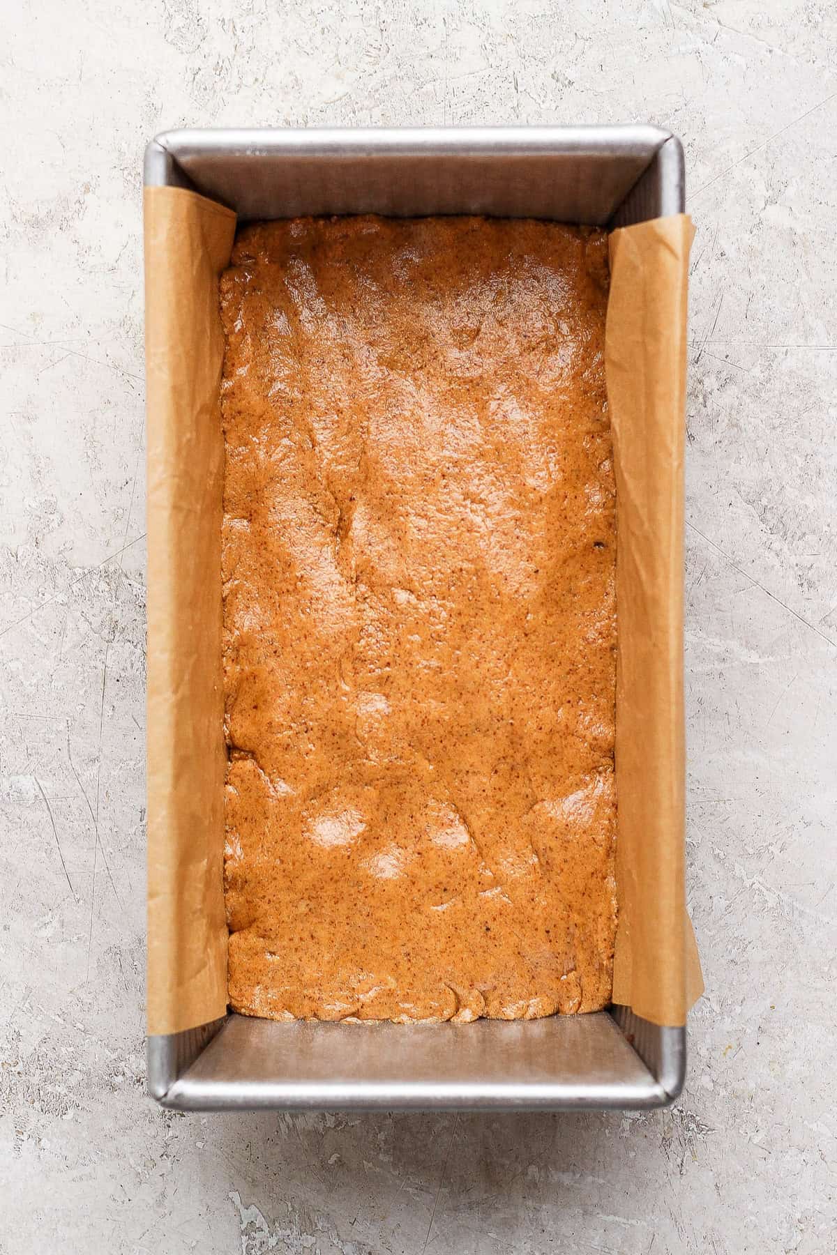 Pressed bar base in a parchment-lined loaf pan before adding the toppings.