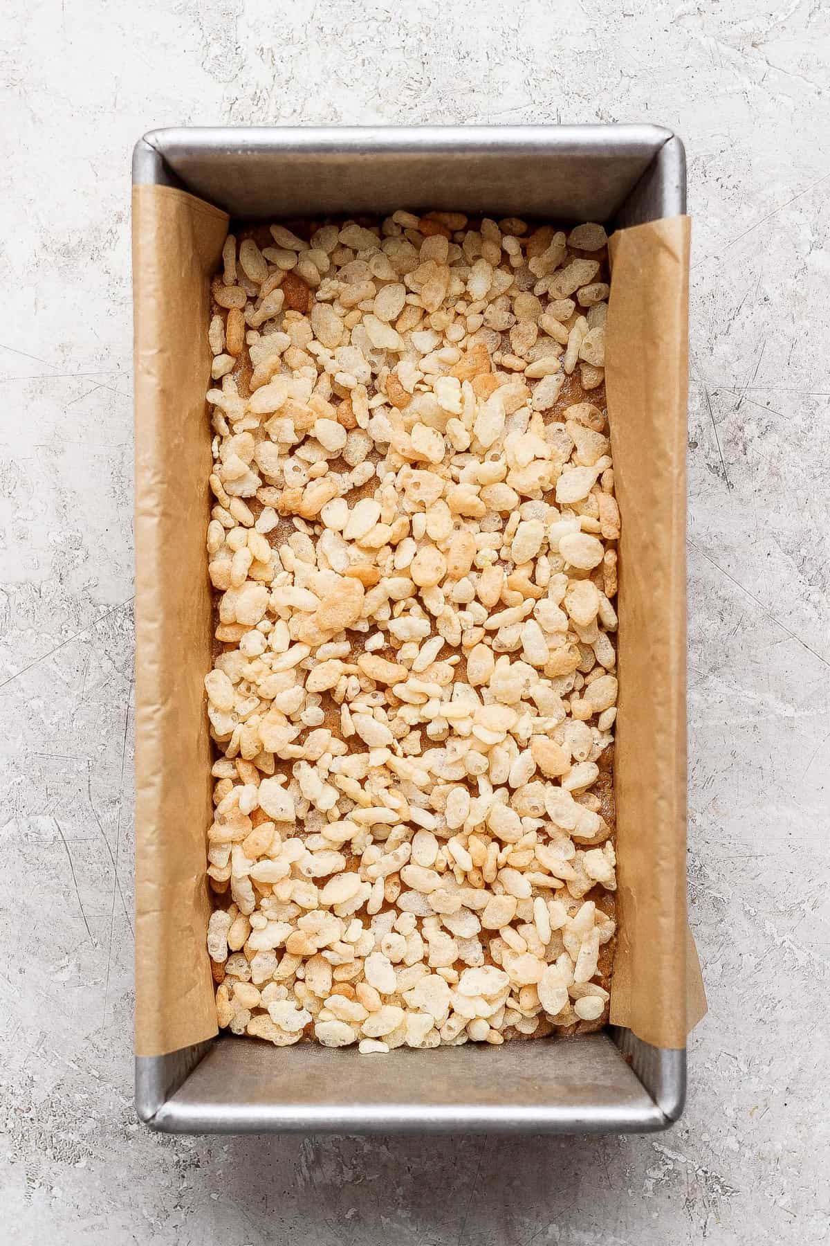 Crispy rice cereal in a parchment-lined loaf pan before the chocolate topping is added.