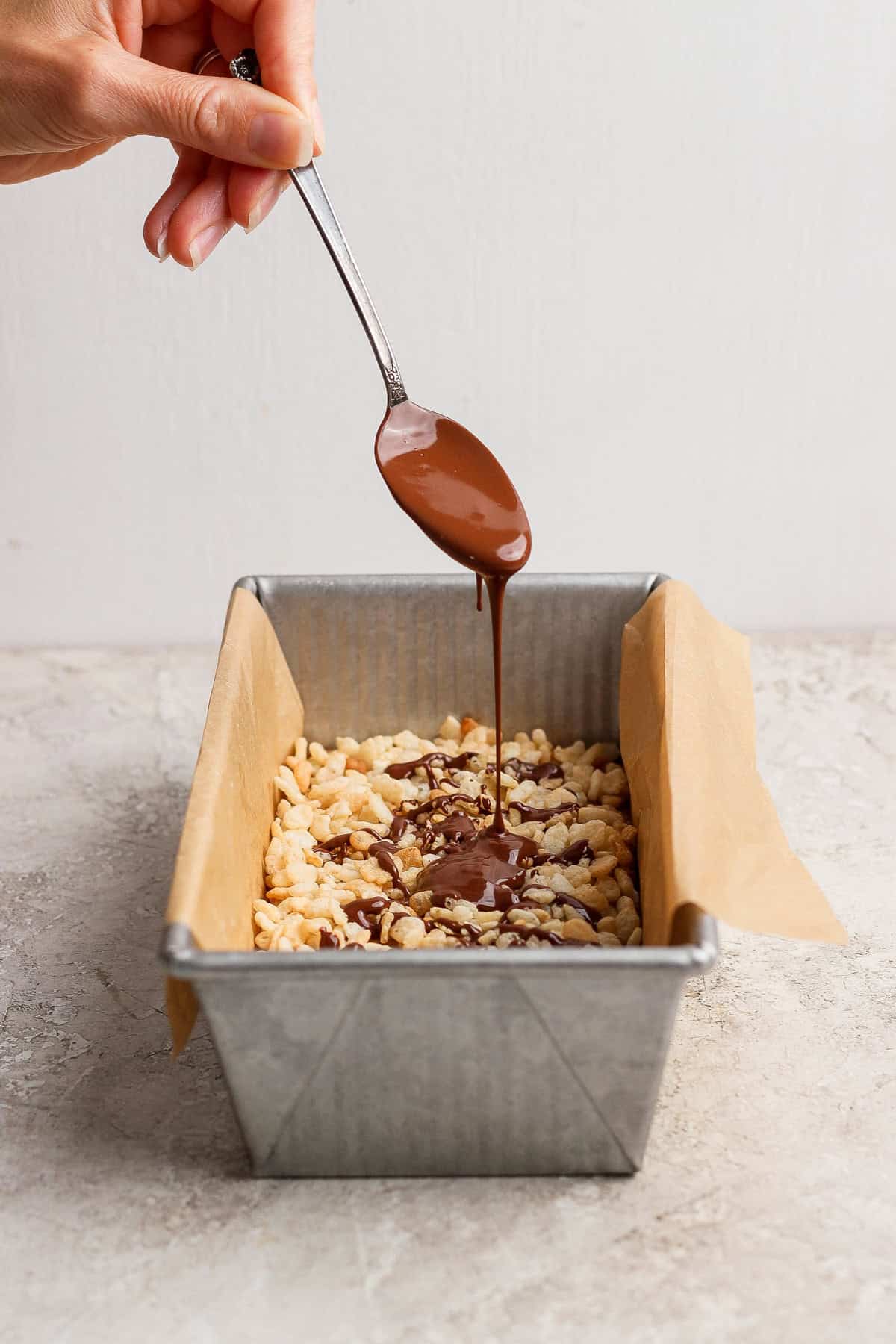 Melted chocolate drizzled over crispy rice cereal in the pan for maple almond butter bars.