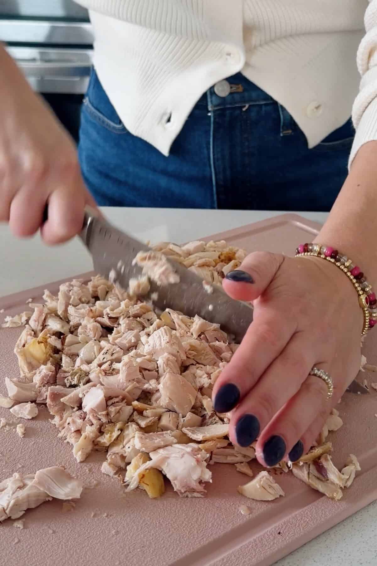 Hands chopping cooked rotisserie chicken on a cutting board.