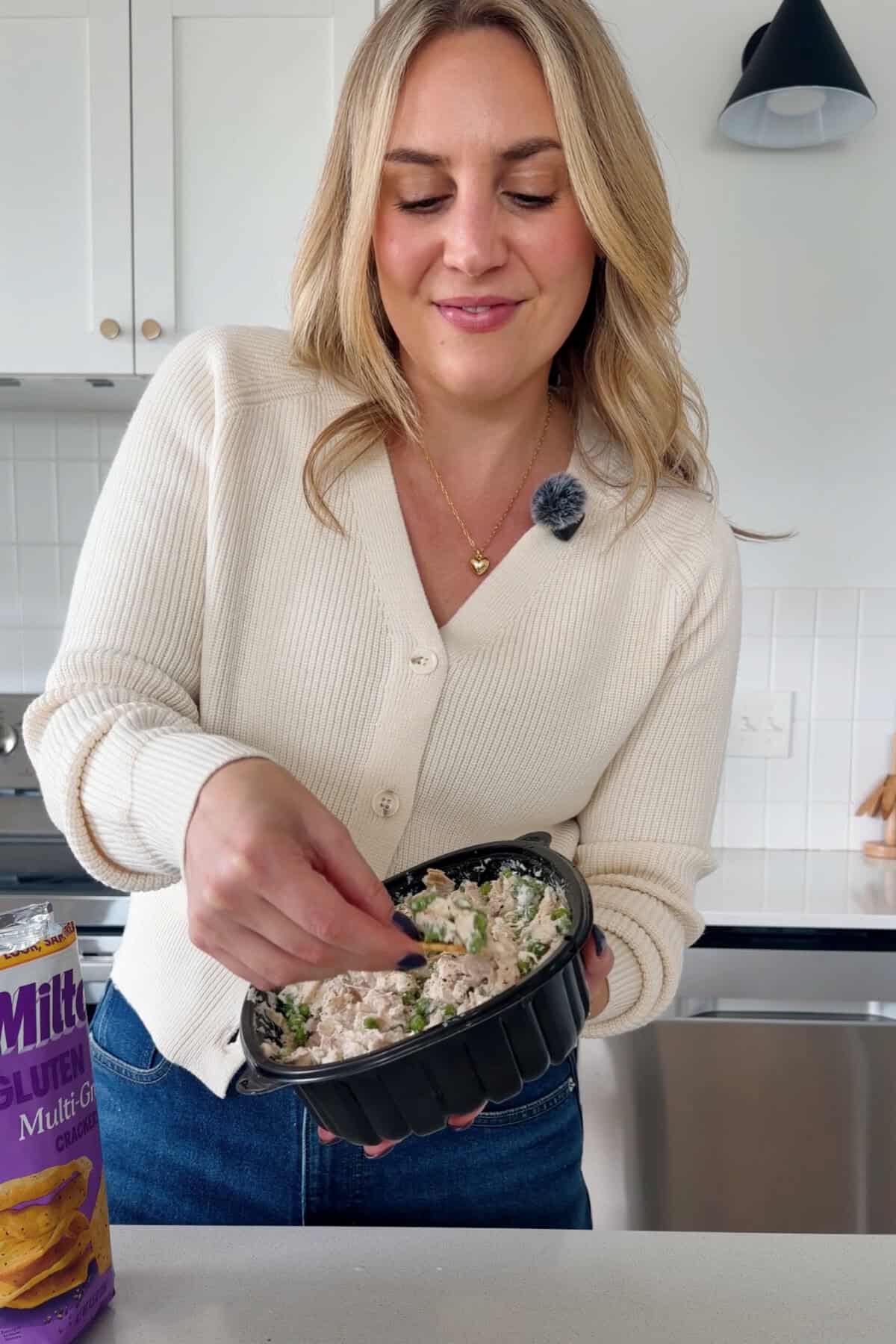 A lidded container holding creamy chicken salad with peas on a kitchen counter.