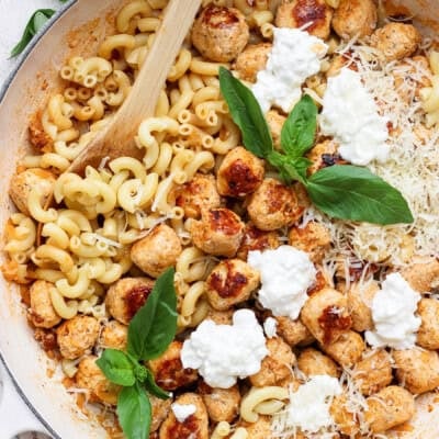 Mini cottage cheese meatballs with elbow pasta, Parmesan, cottage cheese, and fresh basil in a skillet.