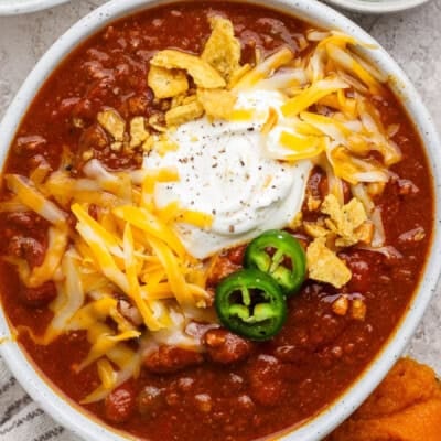 Bowl of slow cooker pumpkin chili with ground beef, kidney beans, sour cream, shredded cheese, jalape&ntilde;o, and tortilla strips.