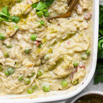 Creamy chicken pesto orzo with peas, sun-dried tomatoes, pesto, and fresh parsley in a white casserole dish.