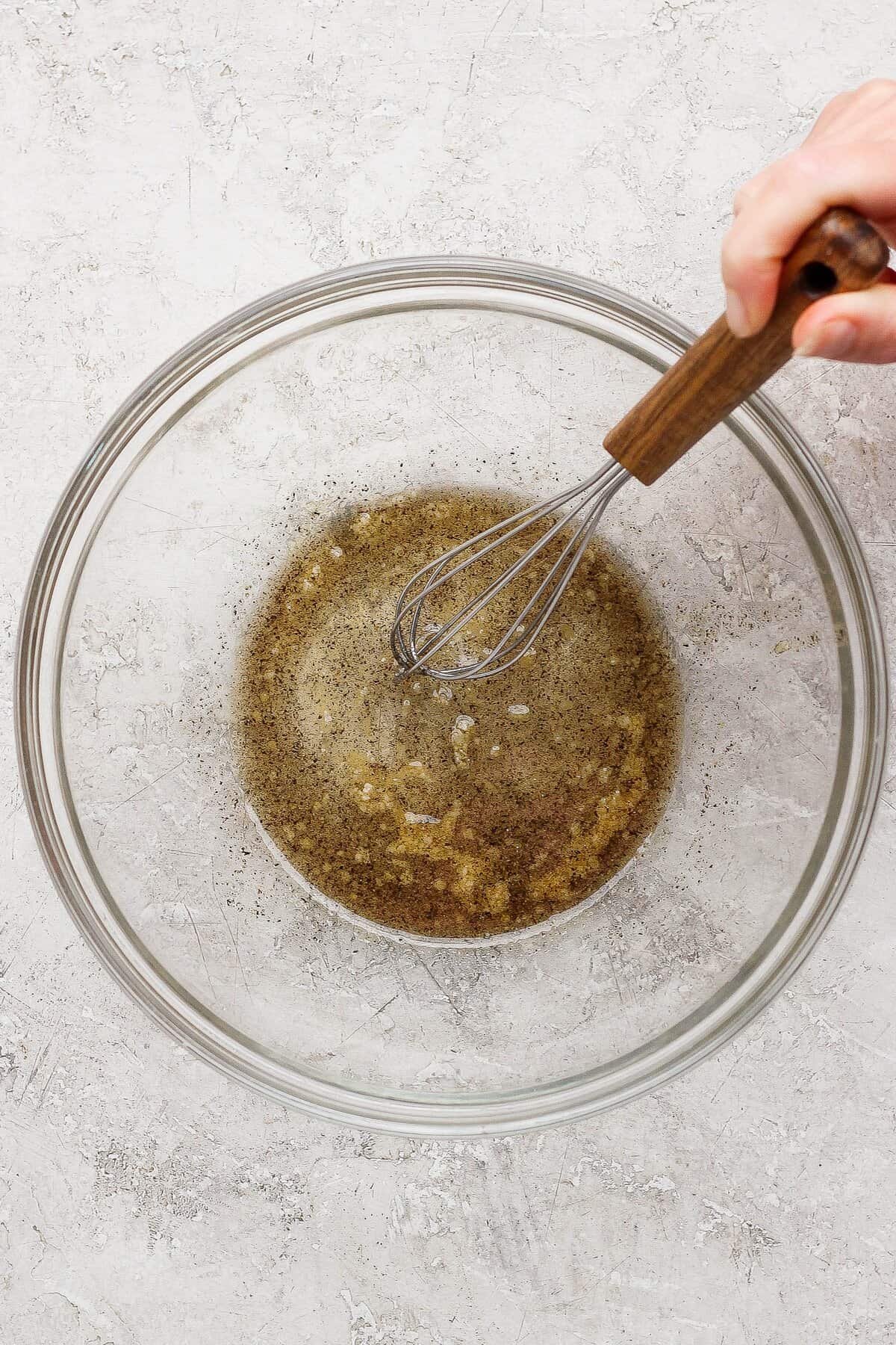 Whisking olive oil, maple syrup, salt, and pepper in a glass mixing bowl.