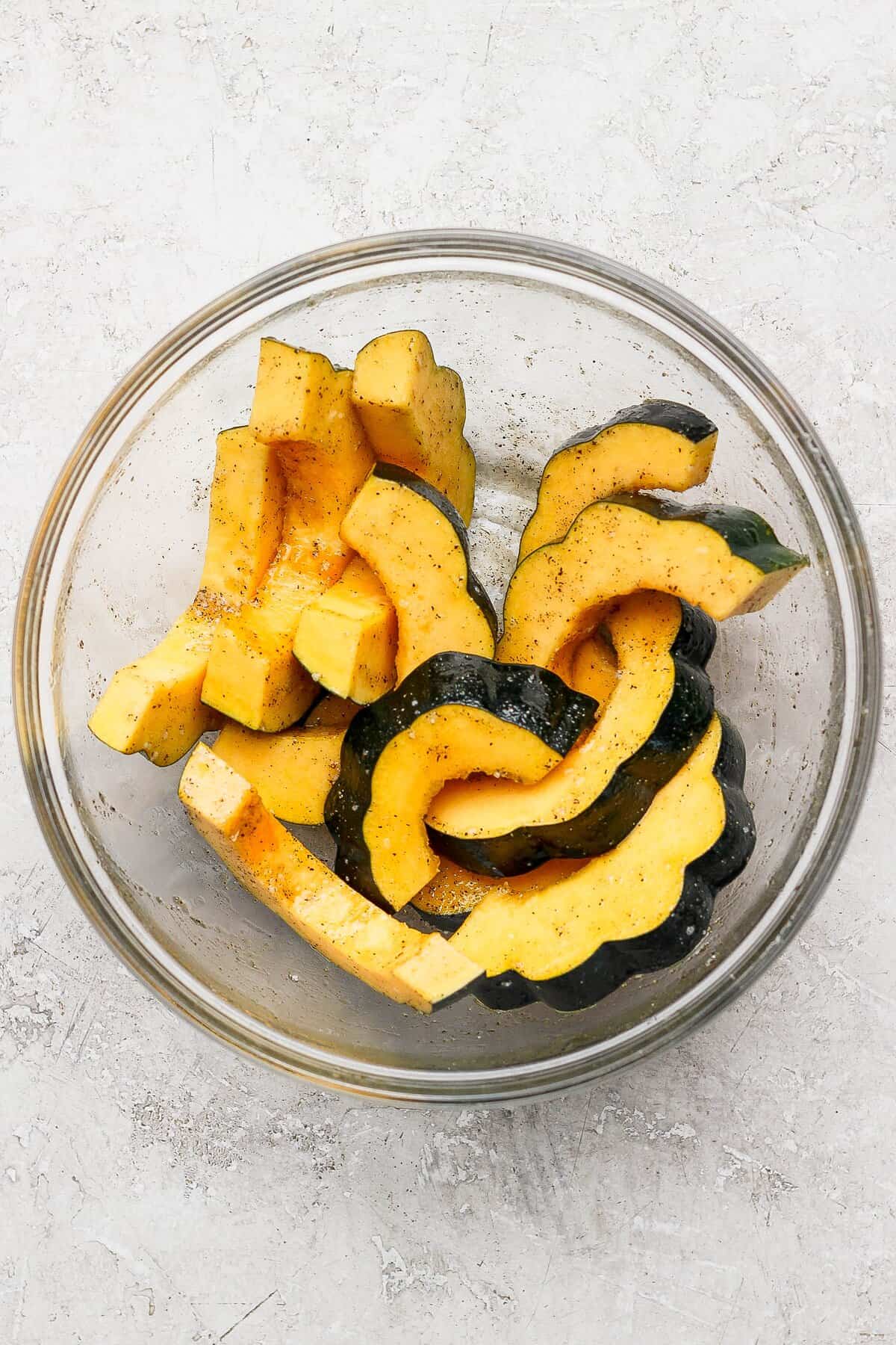 Skin-on acorn squash half-moons in a mixing bowl with the oil and maple syrup mixture.