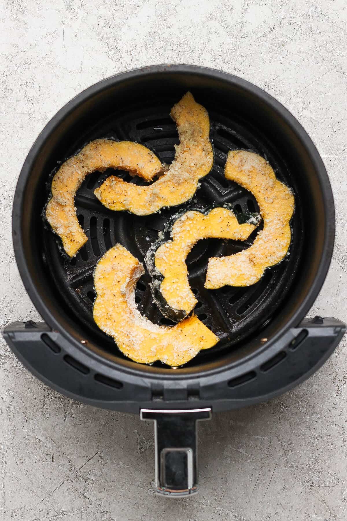 Parmesan-coated acorn squash slices arranged in a single layer in an air fryer basket.