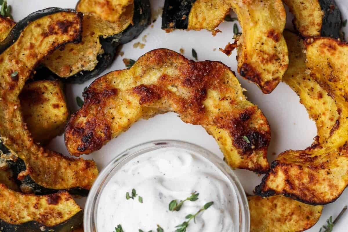 Close-up of Parmesan-coated acorn squash with thyme and a bowl of creamy dip.