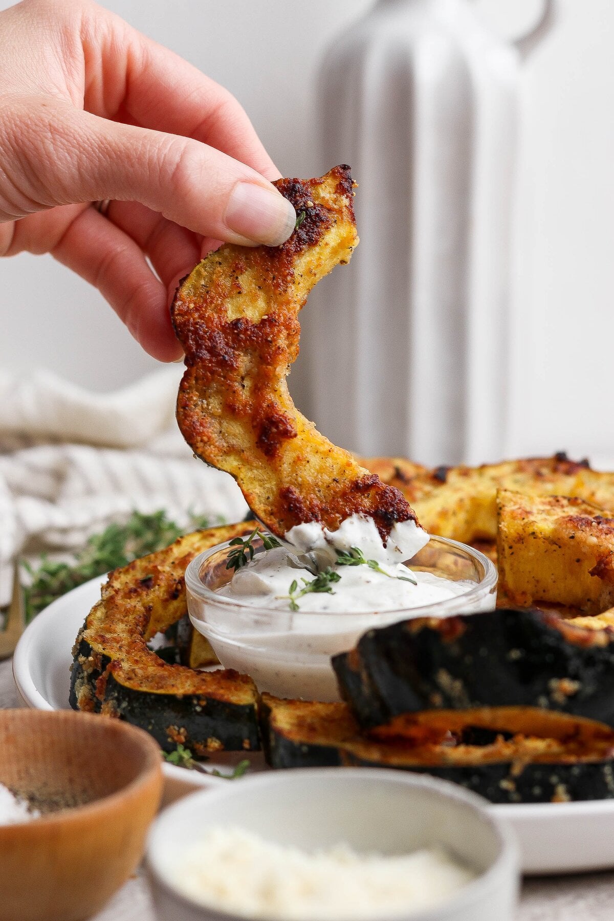 A hand dipping an air-fried Parmesan acorn squash slice into creamy thyme yogurt dip.