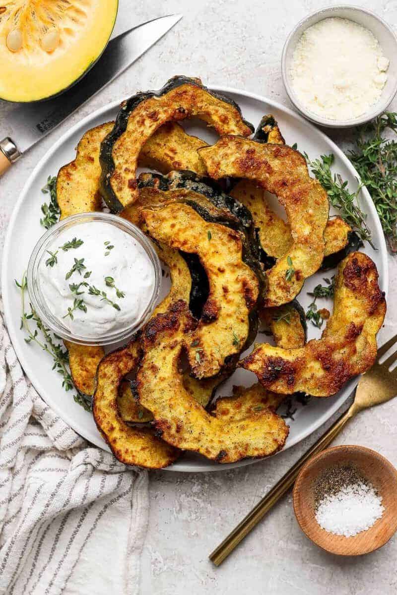 Air fryer Parmesan acorn squash served on a platter with fresh thyme and creamy yogurt dip.