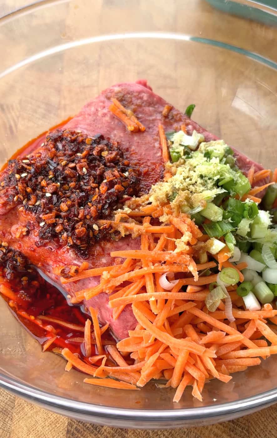 Ground beef, carrots, green onions, garlic, ginger, and chili crunch in a mixing bowl