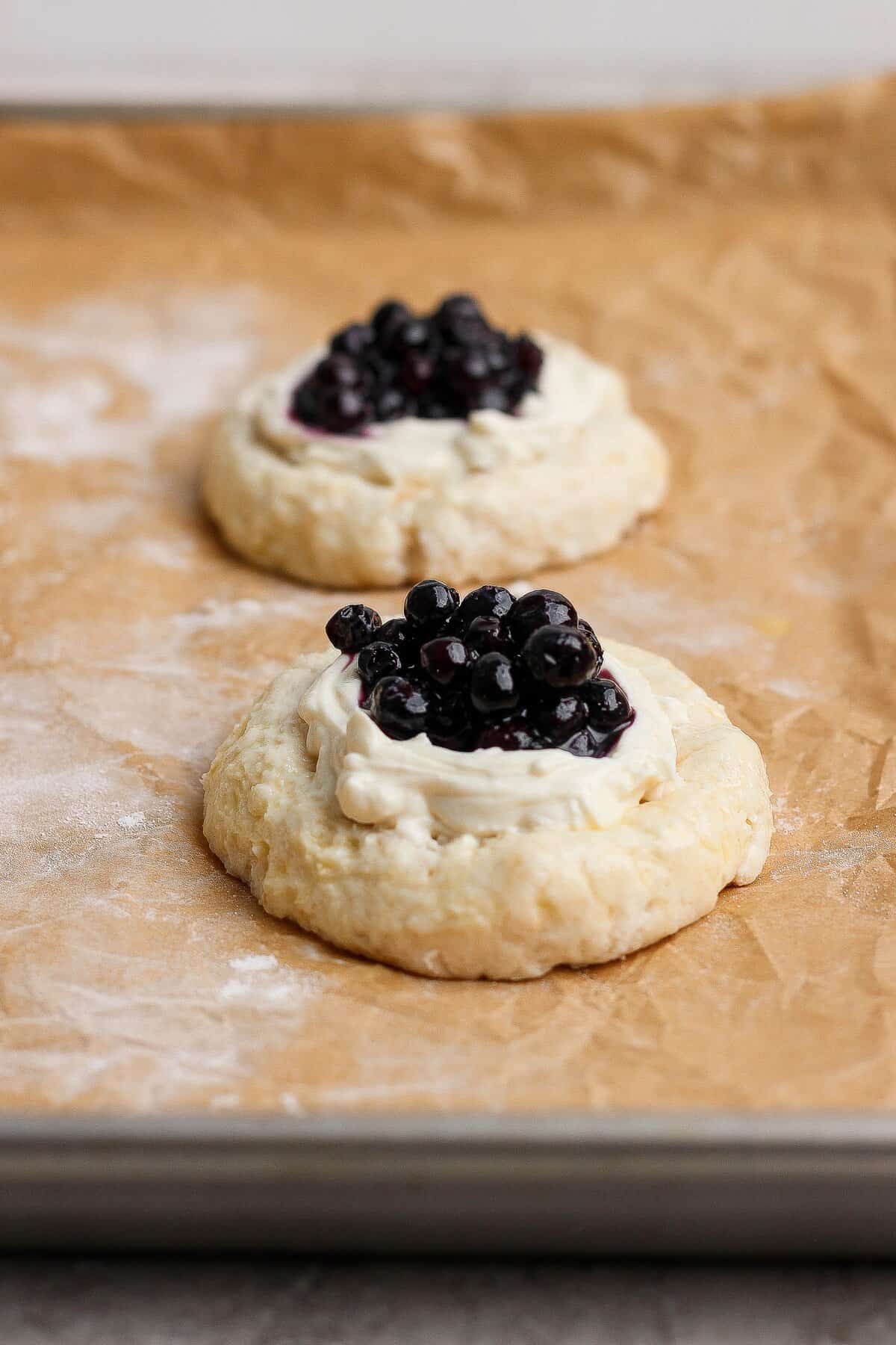 Shaped Danish-inspired dough topped with creamy cheese filling and wild blueberries before baking.