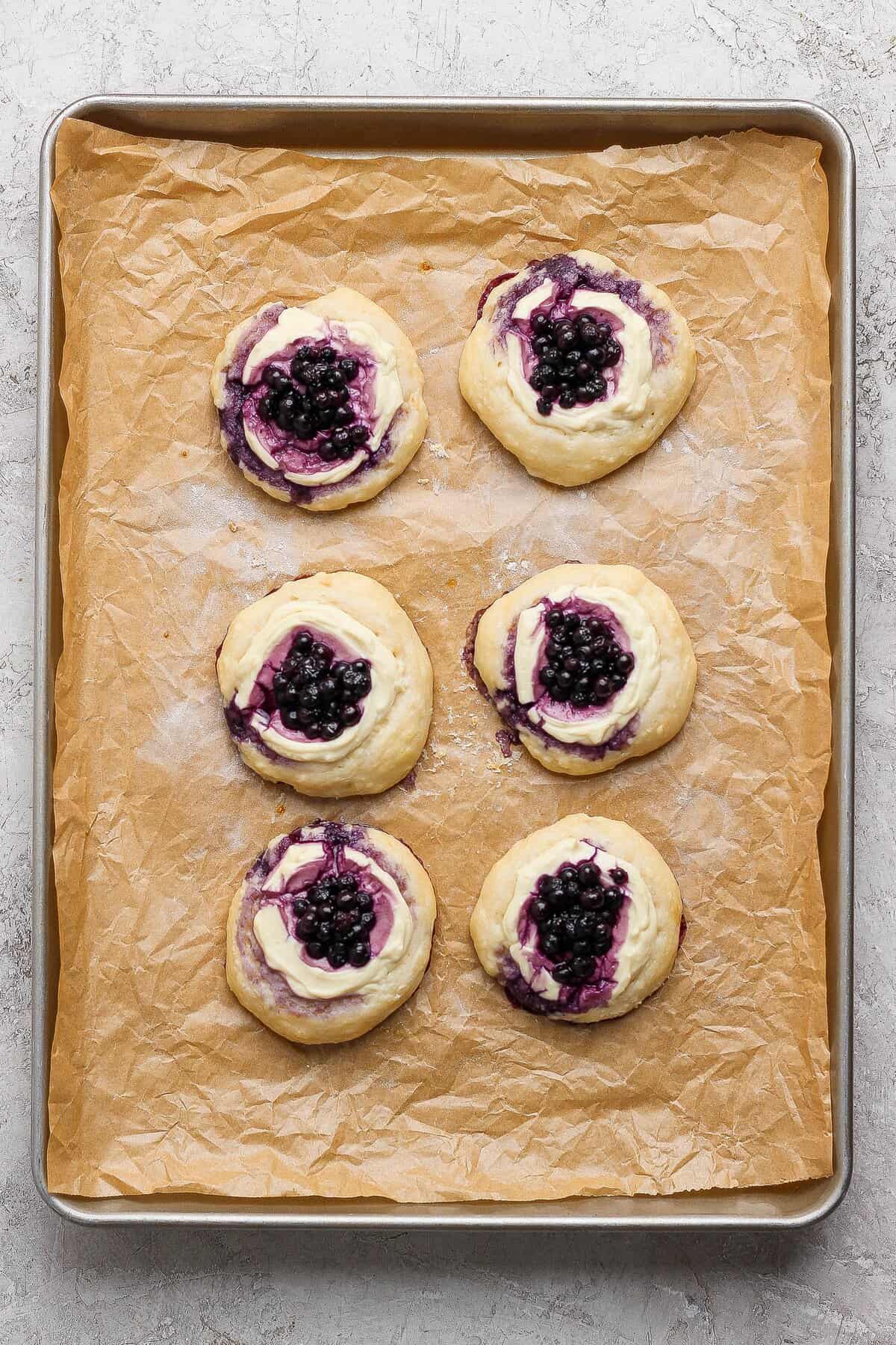 Six blueberry cottage cheese Danish on a parchment-lined baking sheet.