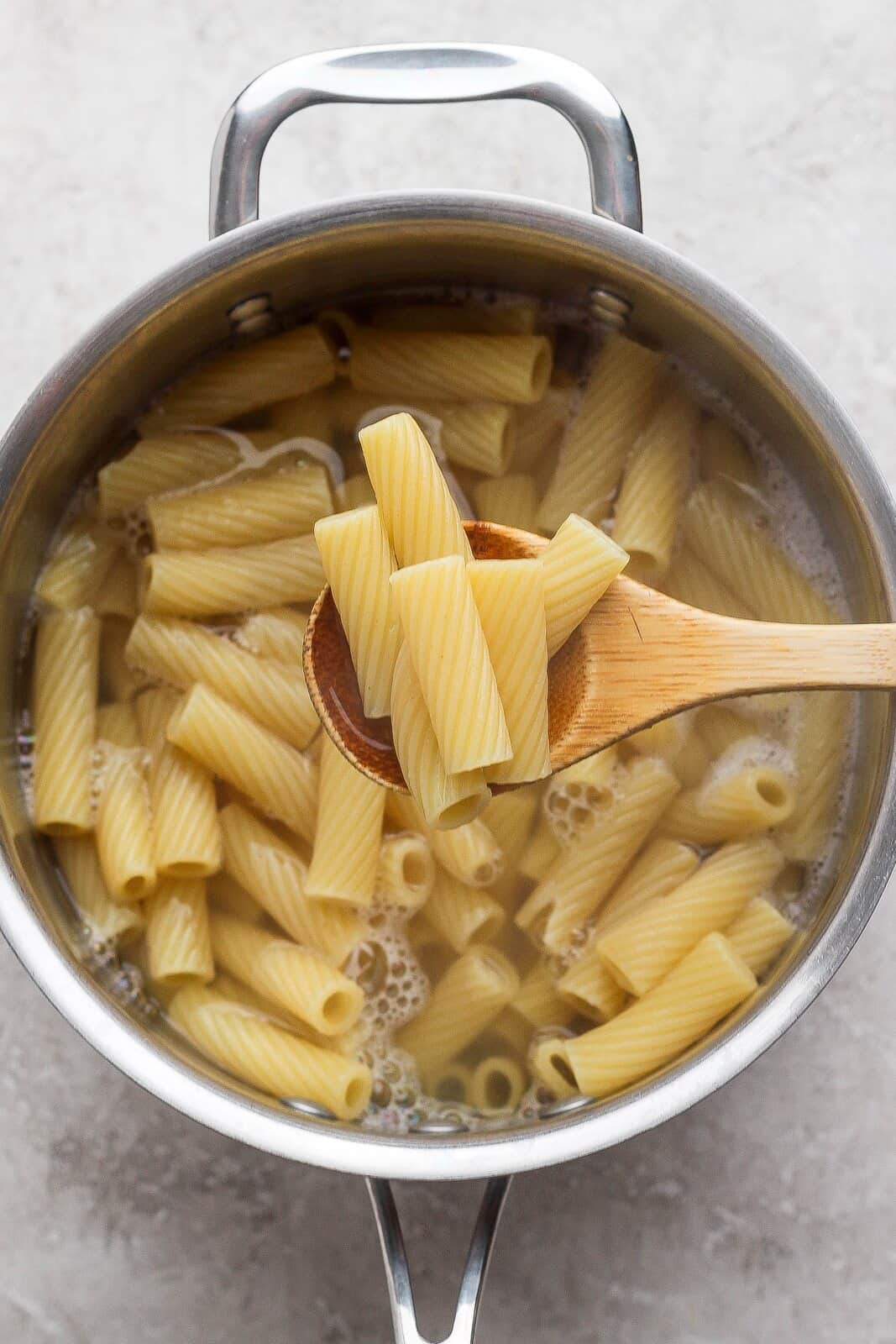 Rigatoni cooking in a pot of water with a wooden spoon.