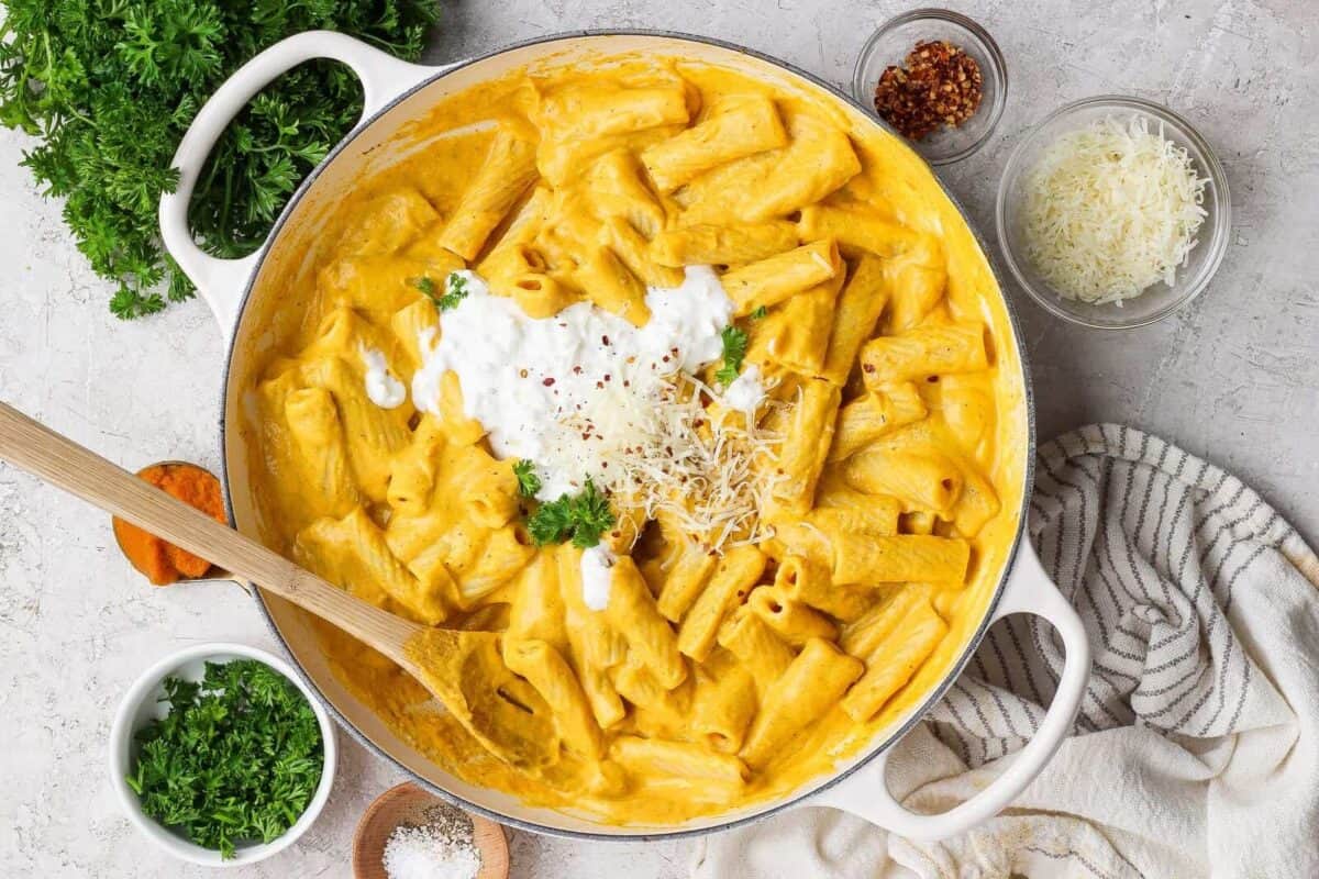 Pumpkin rigatoni in a white skillet topped with cottage cheese, grated Parmesan, red pepper flakes, and green herbs.