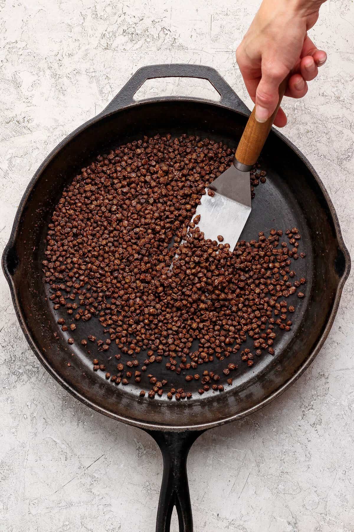 Canned lentils being crisped in a cast-iron skillet with a spatula.