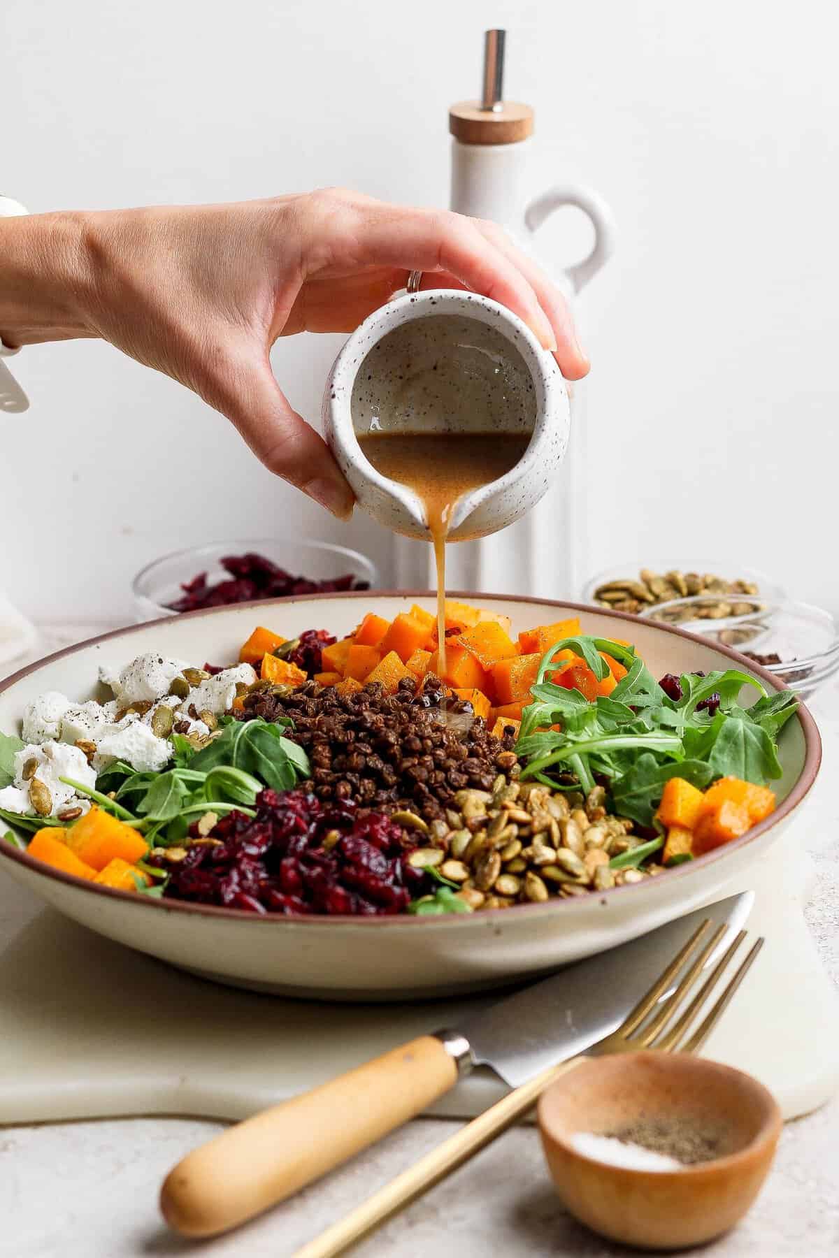 Balsamic-Dijon dressing being poured over a sectioned crispy lentil and butternut squash salad.
