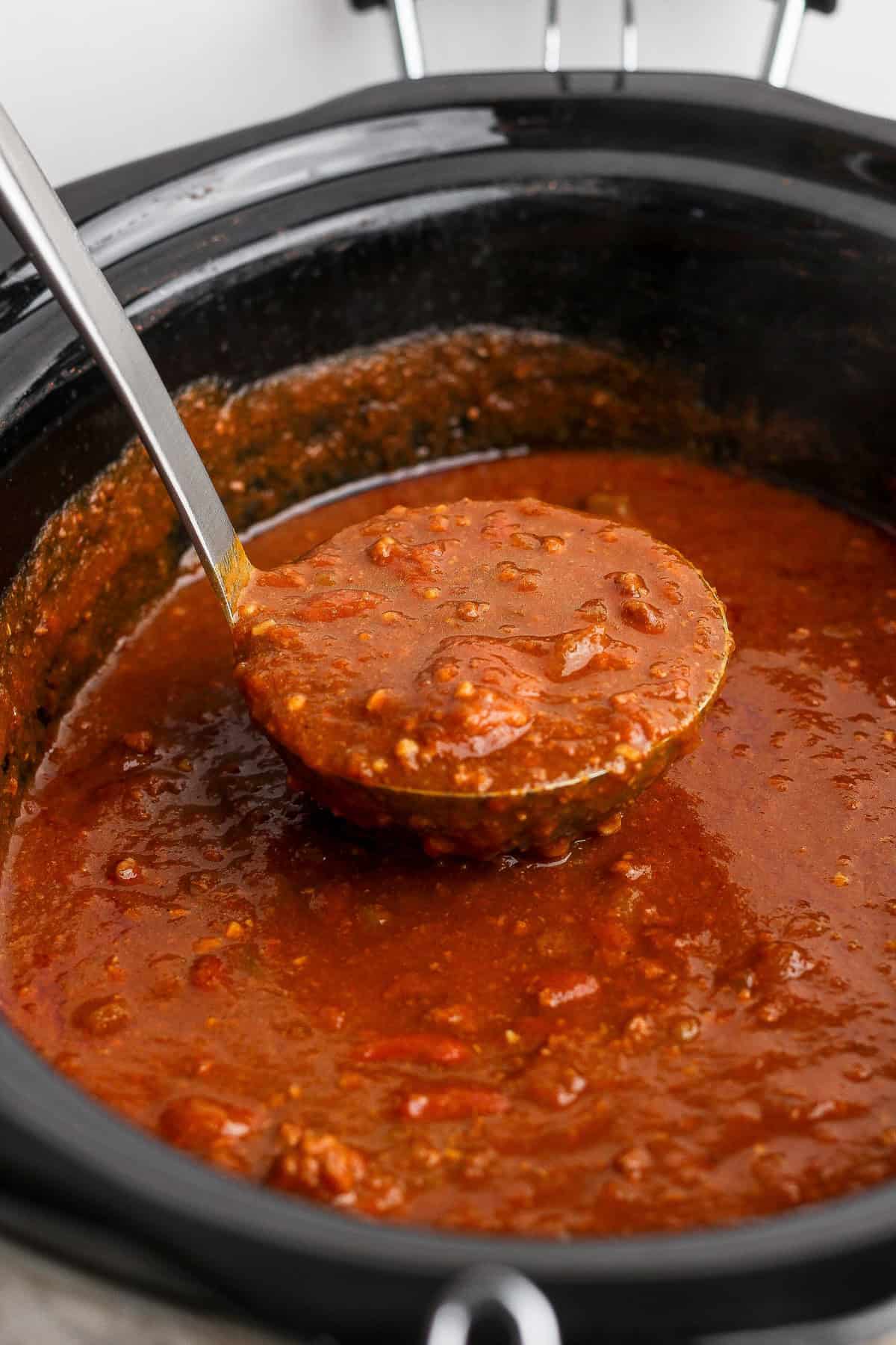 Ladle lifting cooked pumpkin chili with ground beef and kidney beans from the slow cooker.