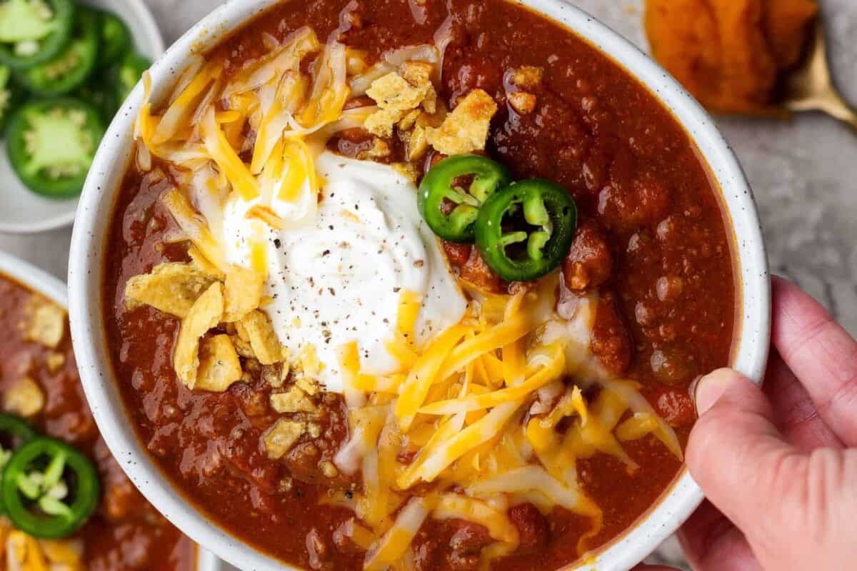 Bowl of pumpkin chili with beef and kidney beans being served with sour cream, cheese, jalape&ntilde;o, and tortilla strips.
