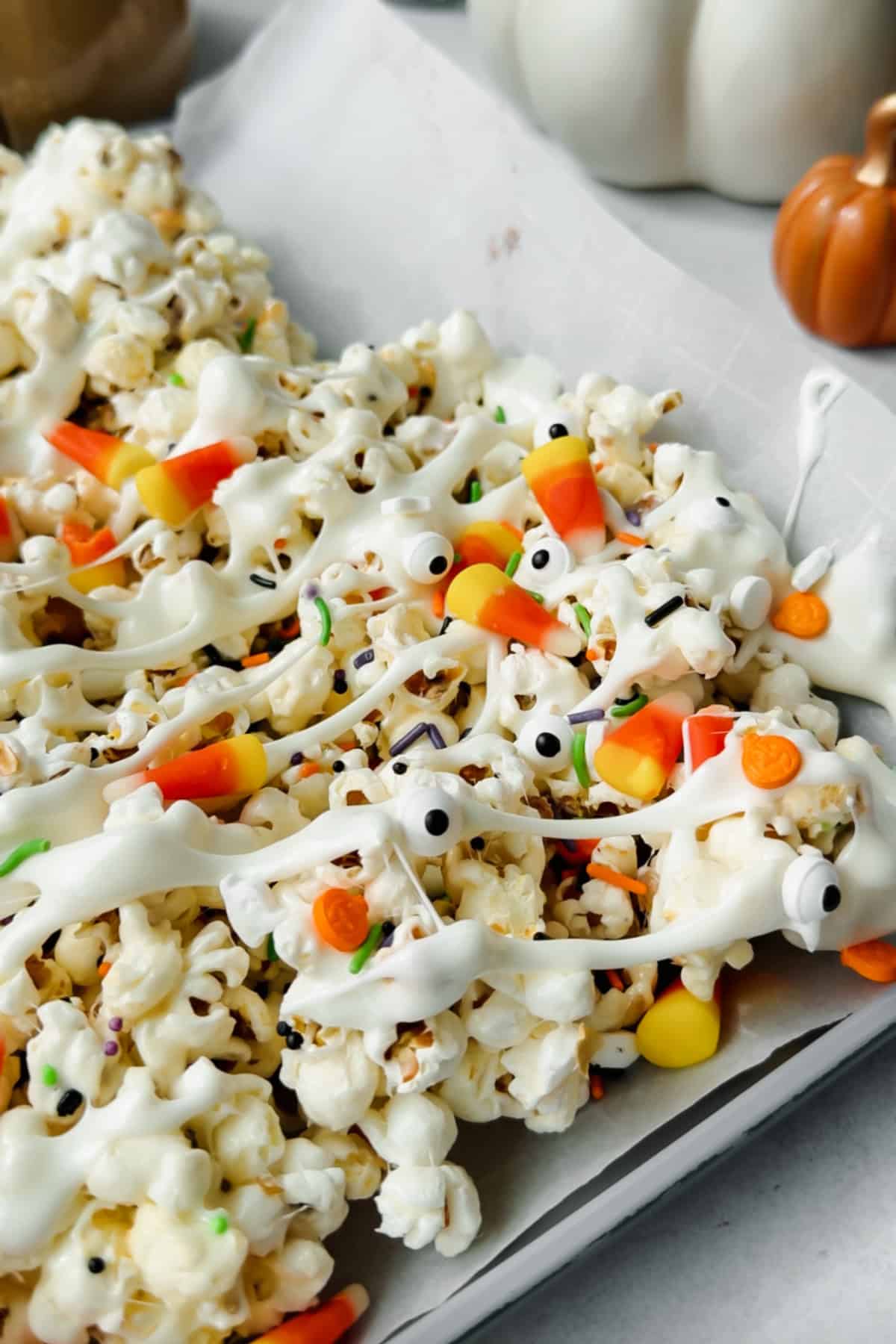 Halloween popcorn on a baking sheet with mummy-style marshmallow drizzle, candy corn, sprinkles, and edible candy eyes.