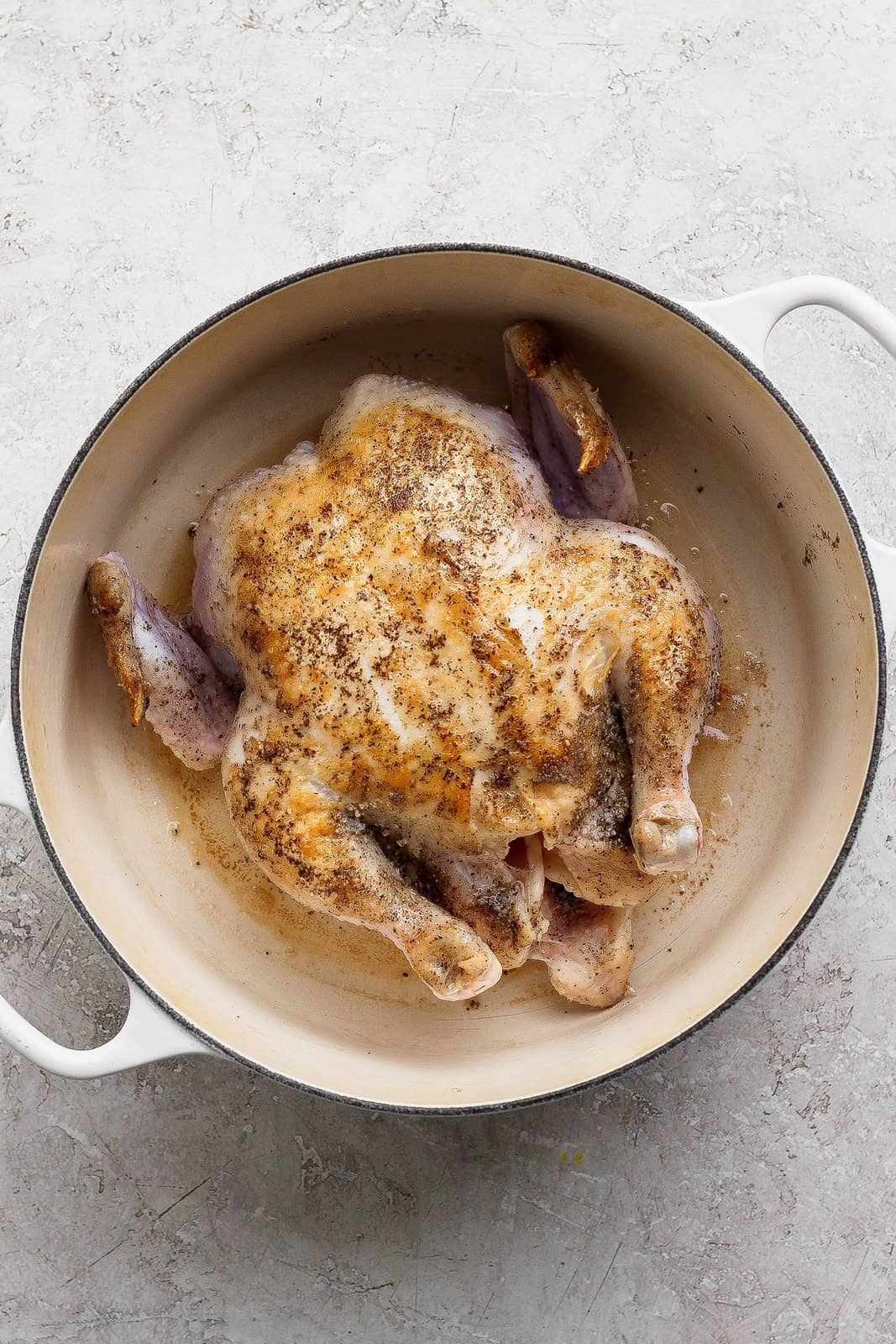 Whole chicken seasoned and browning in a cream-colored Dutch oven after searing.