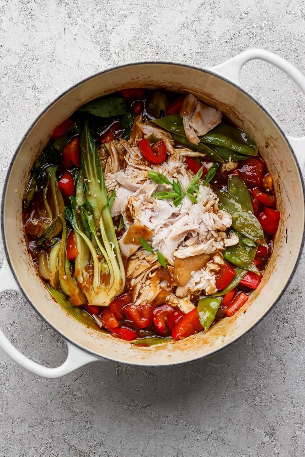 Shredded chicken stirred into glossy sauce with bok choy, snow peas, and red bell pepper in a Dutch oven.