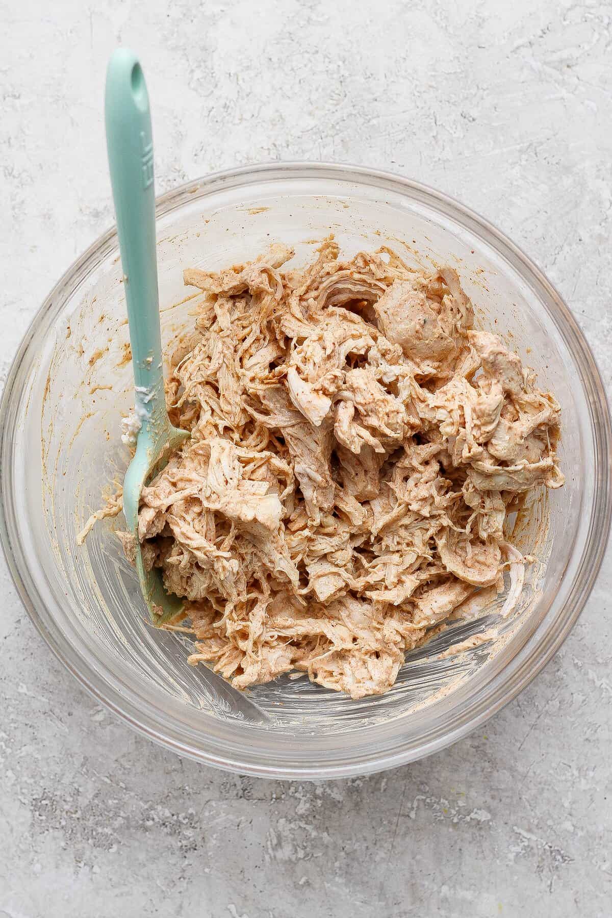 Cooked shredded chicken coated in creamy chili-lime sauce in a glass bowl.