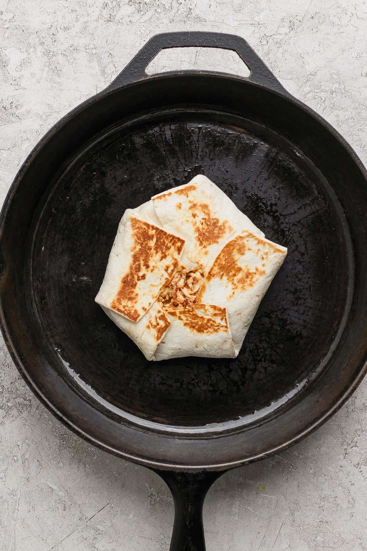 A folded street corn chicken crunchwrap toasted golden brown in a cast-iron skillet.